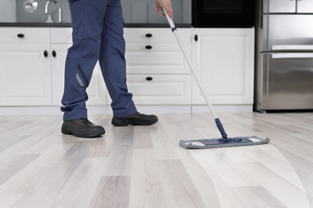 Low Section Of Person Wiping Floor With Mop In Kitchen Room